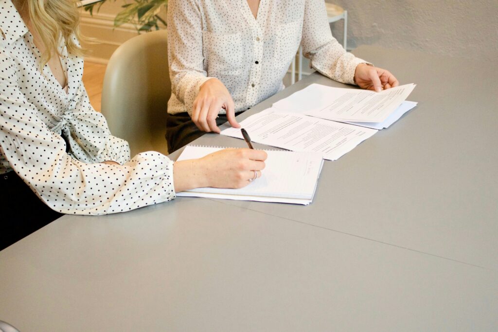 Zwei Frauen sitzen an einem Tisch und schreiben auf weißes Papier